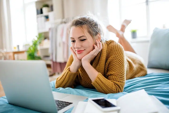 Frau Liegt Laechelnd Auf Bett Schaut Auf Laptop