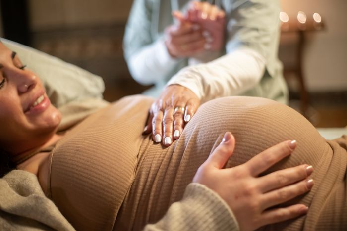 Cropped Image Smiling Pregnant Woman Midwife Home Woman Casual Clothes Lying Bed Midwife Holding Hand Pregnancy Medicine Home Birth Concept