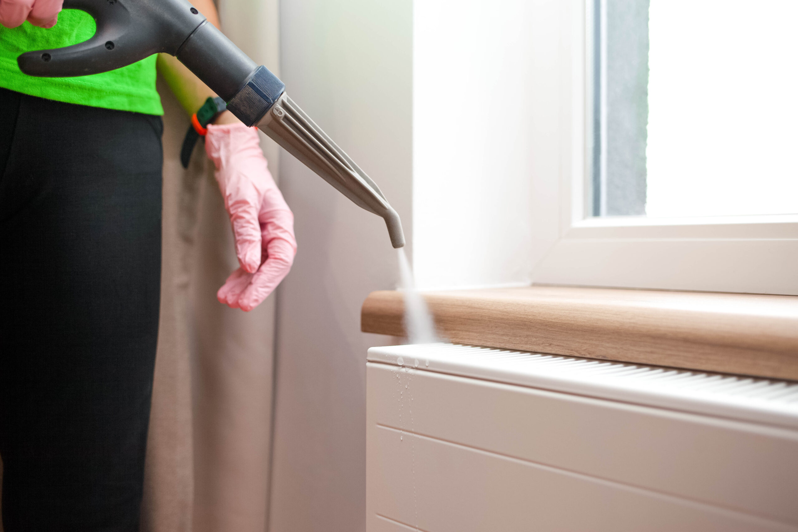 Dampfreiniger putzt Fensterbank, Person mit rosa Handschuhen, reinigungskraft im Einsatz.