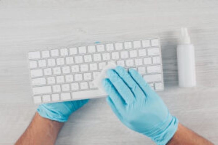 Man Gloves Sanitizing Keyboard Light Wooden Background With Sanitizer 300X200 1
