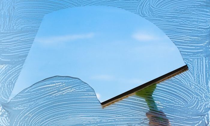 Fensterabzieher reinigt Glas, klare Sicht auf blauen Himmel, Thema: putzen.