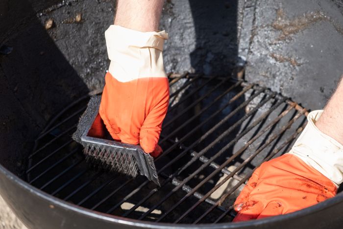 Male Hand With Red Gloves Cleans Round Grill With Stiff Brush