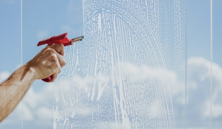 Eine Person betätigt eine Spritzpistole, um Wasser auf ein Glasfenster zu sprühen und so die Sicht und Sauberkeit zu verbessern.