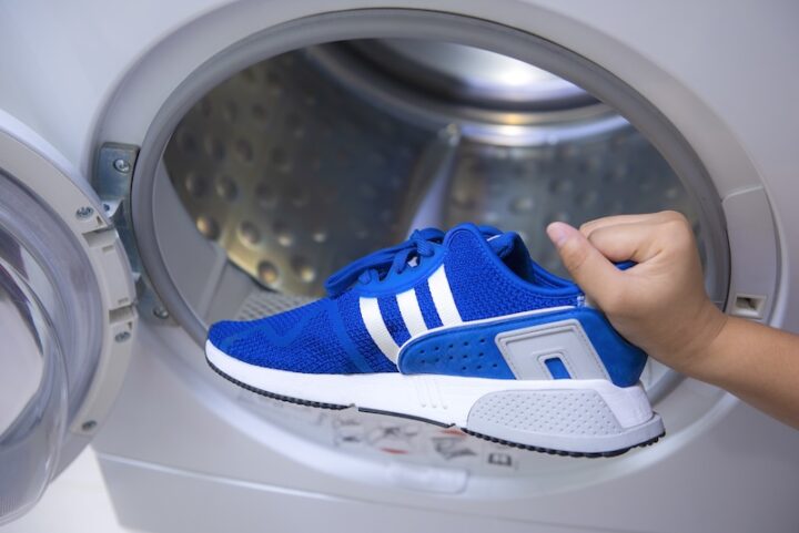 Eine Person, die blaue Adidas-Schuhe zur Reinigung in eine Waschmaschine legt.