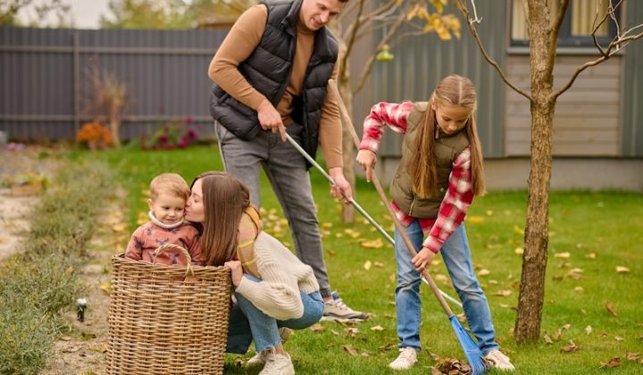 family garden smiling man with school age girl raking leaves young blonde woman crouching kissing cute child basket garden autumn day