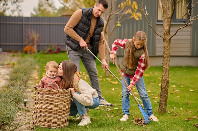 Family Garden Smiling Man With School Age Girl Raking Leaves Young Blonde Woman Crouching Kissing Cute Child Basket Garden Autumn Day