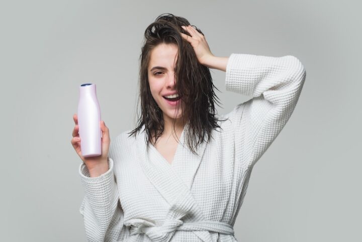 A woman is holding a pink a shampoo bottle, ready to style her hair.