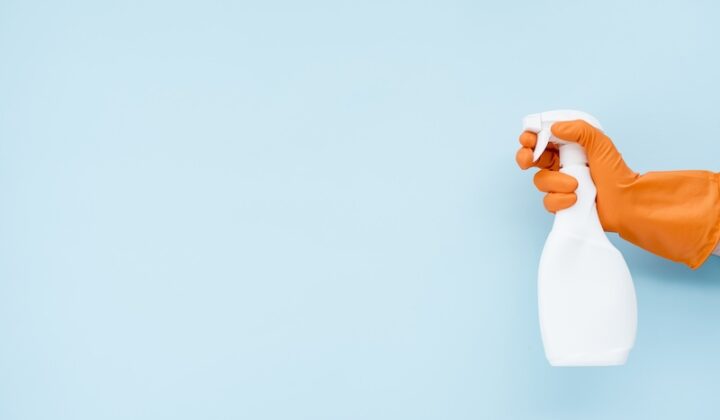 Eine Hand mit Gummihandschuhen hält eine weiße Sprühflasche.