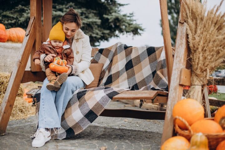 A woman and child enjoy a swing surrounded by pumpkins in a vibrant autumn setting.