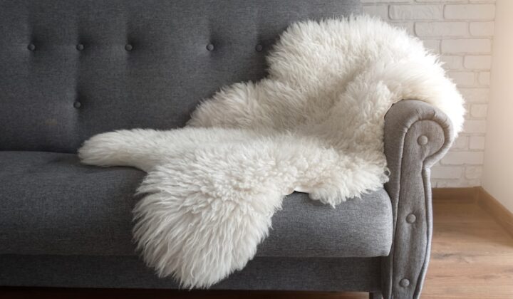 Auf einer Couch vor einem Fenster liegt ein weicher Schaffellteppich, der Gemütlichkeit ausstrahlt.