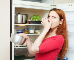 A woman holds a bowl while standing in front of an open refrigerator, examining its contents.