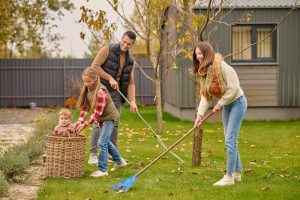 working mood smiling young man pretty woman warm clothes raking leaves lawn girl with little brother pouring into basket garden near house