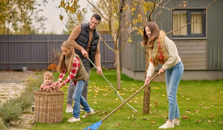 working mood smiling young man pretty woman warm clothes raking leaves lawn girl with little brother pouring into basket garden near house