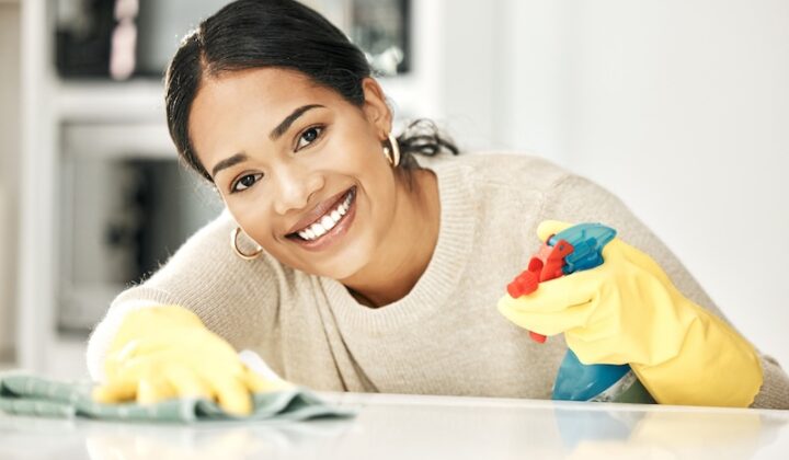 Eine Frau mit Gummihandschuhen lächelt, während sie eine Arbeitsplatte reinigt.