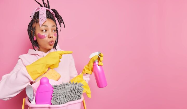 Eine junge Frau trägt ein pinkes Shirt und hält einen Eimer voller Putzmittel.