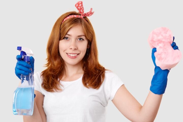 A Woman Holds A Cleaning Product In One Hand And A Sponge In The Other, Ready To Clean A Surface.