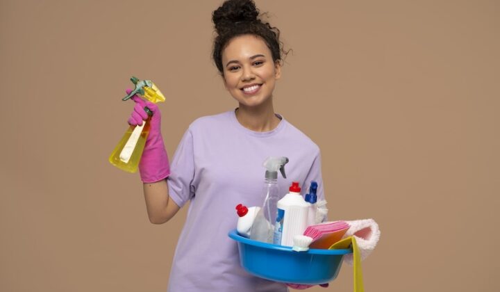 Cheerful young woman with cleaning supplies and products, preparing to tackle household chores.