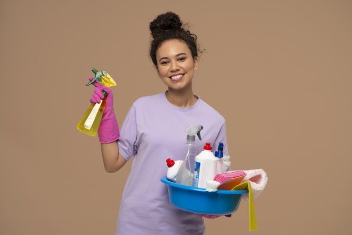 Cheerful young woman with cleaning supplies and products, preparing to tackle household chores.