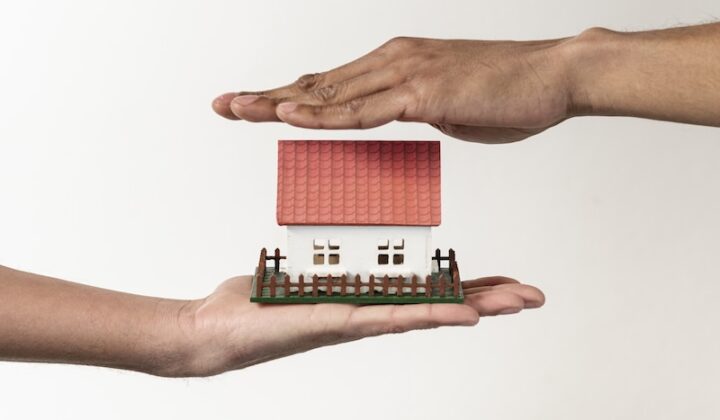 Zwei Hände halten ein kleines Modell eines Hauses.