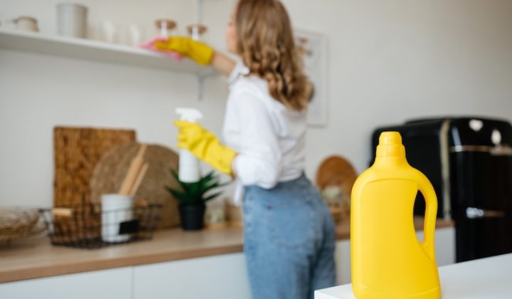 Eine Frau reinigt die Küche mit einer gelben Flasche.