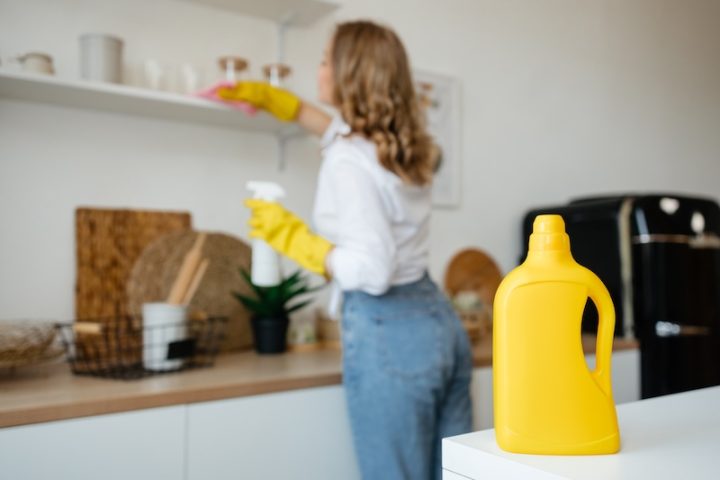 Eine Frau reinigt die Küche mit einer gelben Flasche.