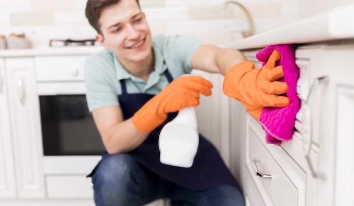 Ein Mann mit Handschuhen und Schürze reinigt eine Küche.