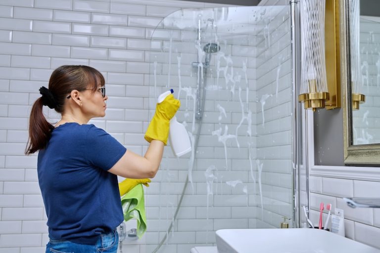 woman cleaning bathroom washing glass shower
