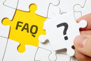 A hand holds a white puzzle piece with a question mark, above a yellow space labeled "FAQ." The image suggests solving questions or uncertainties.