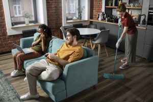 people sitting in a living room with one of them cleaning the floor