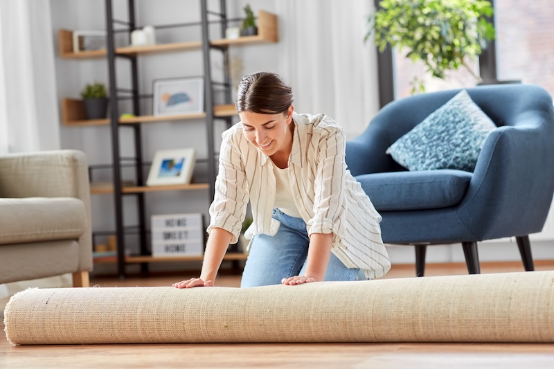 Young Woman Unfolding Carpet Home