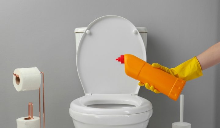 woman cleaning a toilet with detergent in a bathroom closeup image