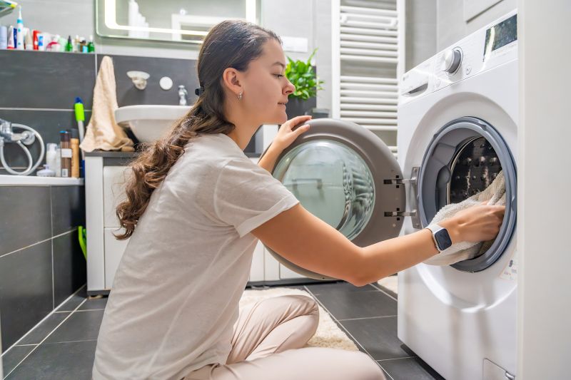 Young Woman Inserting Clothes Inside Washing Machine Home Bathroom