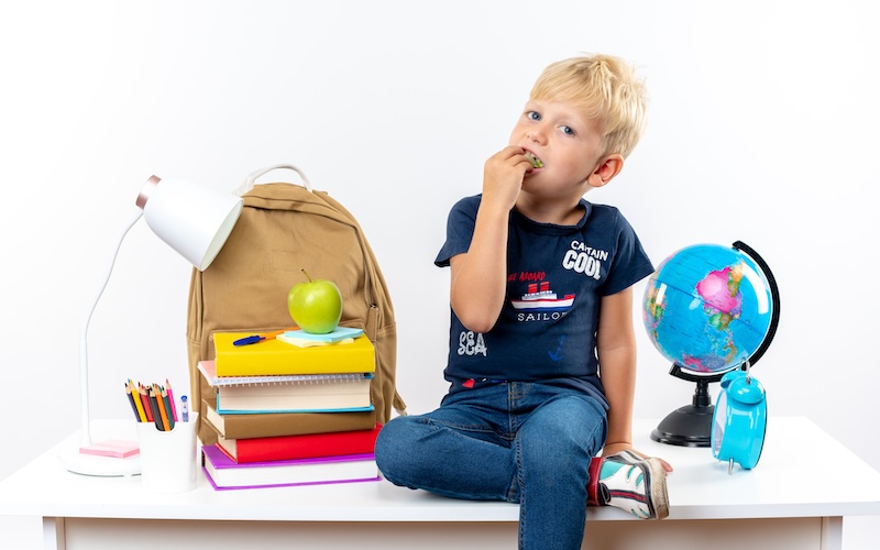 Little School Boy Sitting Table With School Tools Eating Piece Apples