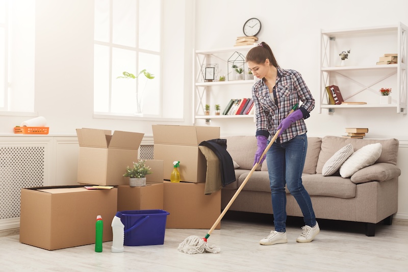 New Home Cleaning Young Woman Tiding Up After Moving New Appartment Girl With Various Detergents Rags Mops Living Room Full Carton Boxes Household Spring Cleanig Concept