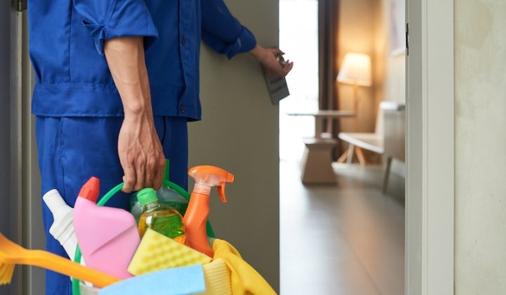 unrecognizable cleaner walking into hotel room with tools detergents